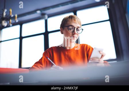 Student reading message on smartphone doing homework sitting at table Stock Photo
