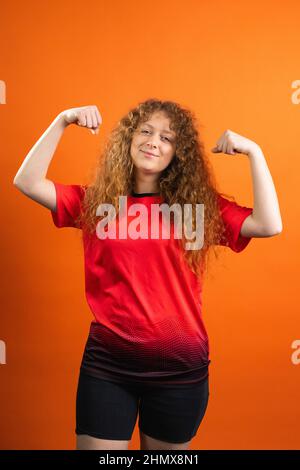 Strong redhead young woman fan of football in team uniform red and black color posing for the camera with satisfied facial expression. Stock Photo