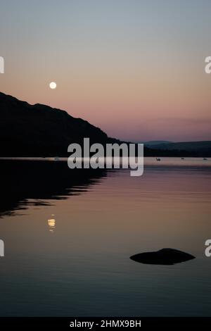 The rising Wolf moon, first full moon of 2022, after sunset captured from Ullswater, Lake District, Cumbria, UK on 17th January 2022 Stock Photo