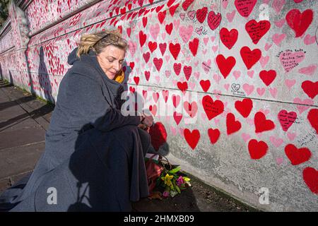 Female writing names on The National COVID Memorial Wall painted with red hearts on beautiful sunny day . Westminster, London , UK .