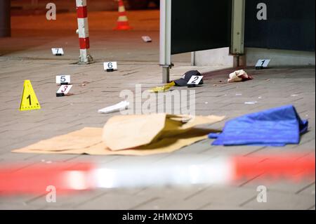 Hamburg, Germany. 12th Feb, 2022. Numbered evidence boards stand next to traces of blood and a cap at the cordoned-off location where the injured man was found in front of a shopping center. According to police, a man was injured 'not insignificantly' in a knife attack in Hamburg-Harburg. The homicide squad is investigating, said a spokesman for the police situation center after the crime on Saturday evening. Credit: Jonas Walzberg/dpa/Alamy Live News Stock Photo