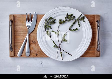 White ceramic plate and dry mint leaves and a tray with cutlery Stock Photo