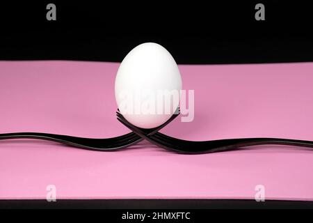 White raw egg balanced on two black forks on pink Stock Photo