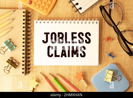 Jobless claims text on white paper from a notepad on a wooden background. wooden blocks magnifier Stock Photo