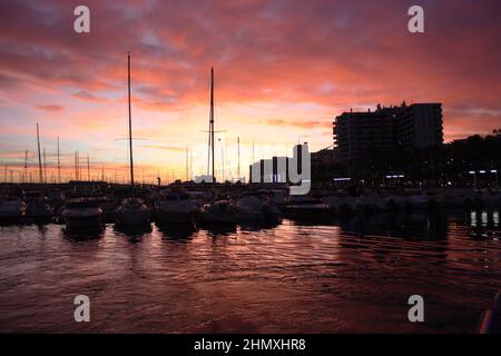 fiery red and purple sunset on ibiza coast view from port at balearic sunset between boats Stock Photo