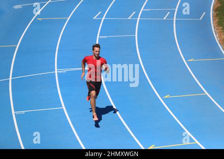 Running man professional athlete runner working out on track and field sport stadium. Top view of male sports person training hiit workout in Stock Photo