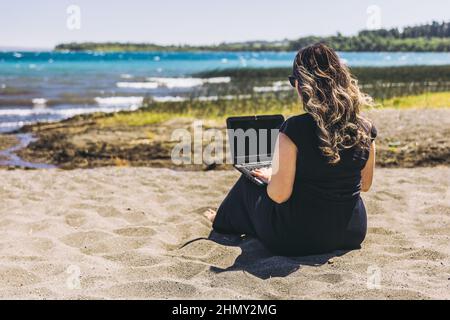 Young woman doing remote online work from the beach. Teleworking concept.  Stock Photo