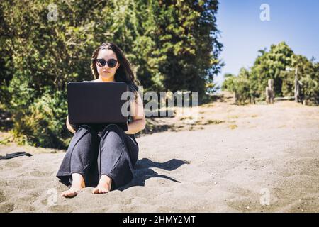 Young woman doing remote online work from the beach. Teleworking concept.  Stock Photo