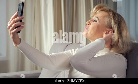 Elderly blonde woman takes selfies using cellphone Stock Photo