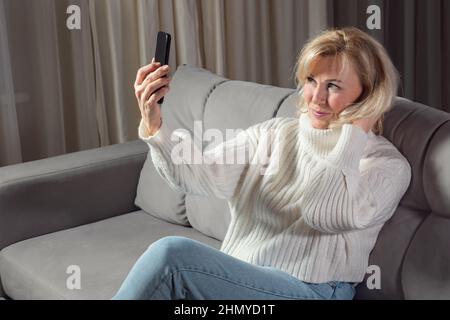 Elderly blonde woman takes selfies using cellphone Stock Photo