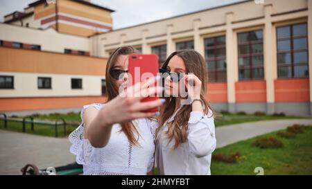 Two girls schoolgirls make a selfie using a smartphone against the background of the school. Stock Photo
