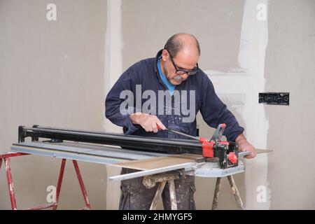 Senior contractor cutting a ceramic wood effect tile with a manual tile cutter. Stock Photo
