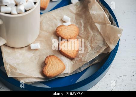 cookies in the form of hearts on a blue tray, against the background of coffee with marshmallows. valentine's day concept Stock Photo