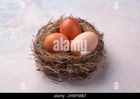 Three chicken eggs in a nest on a light background. Top view, close-up. Stock Photo