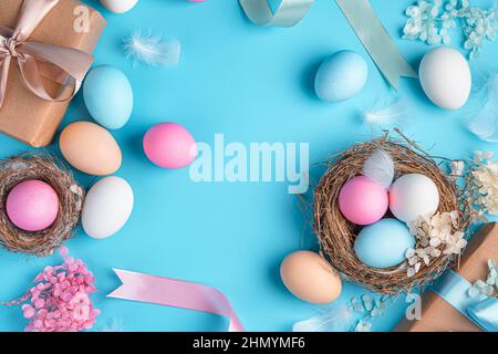 Easter background with colored eggs, nests, ribbons and feathers on a blue background. Top view, copy space. Happy Easter. Stock Photo