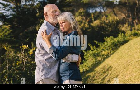 Mature couple slow dancing in a park. Romantic elderly couple enjoying the sun in each other's arms. Affectionate senior couple spending quality time Stock Photo