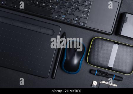 Top view of designer work place with graphics tablet, memory card, keyboard, portable hard drive on black background Stock Photo