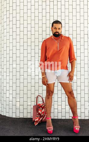 Stylish drag queen looking at the camera while standing against a white background. Non-conforming young man wearing make up and jewellery. Young man Stock Photo