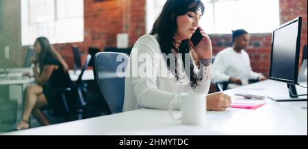 Focused businesswoman taking an important phone call in the office. Creative businesswoman connecting with her business clients in a modern office. Yo Stock Photo