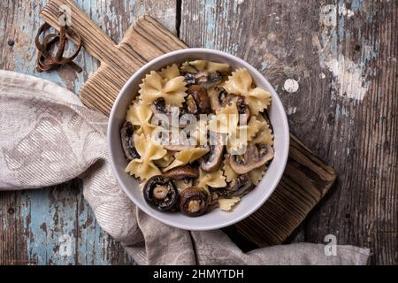 Top view of tasty italian farfalle pasta and champignon mushrooms with cream sauce in bowl on rustic wooden background Stock Photo