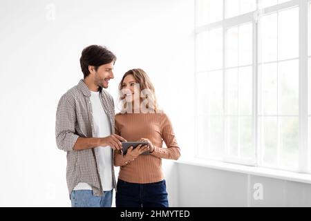 Cheerful european young man and lady in empty room with panoramic window, hold tablet and planning design Stock Photo