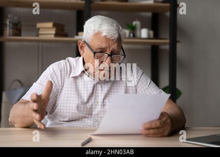 Confused frustrated elder senior 80s man in glasses reading document Stock Photo