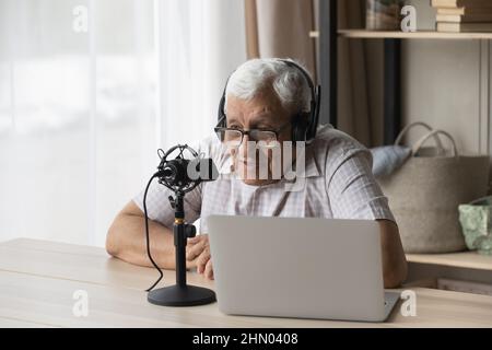 Elder radio host in headphones and glasses speaking at microphone Stock Photo