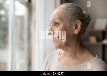 Happy thoughtful mature 70s woman looking out of window Stock Photo