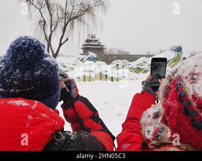 Beijing, China. 13th Feb, 2022. People take pictures of the snow view near a turret of the Palace Museum, also known as the Forbidden City, in Beijing, capital of China, Feb. 13, 2022. A snowfall hit Beijing on Sunday. Credit: Ding Hongfa/Xinhua/Alamy Live News Stock Photo