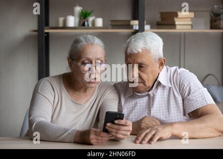 Focused old grandparents couple sharing mobile phone Stock Photo