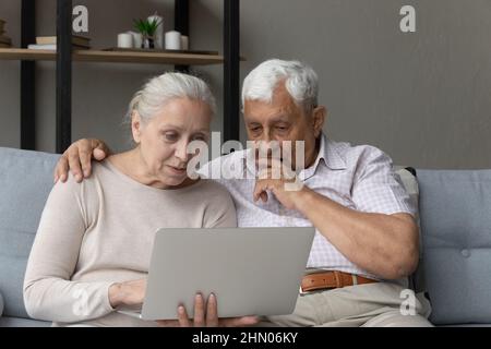 Focused serious elder couple using online app, banking service Stock Photo