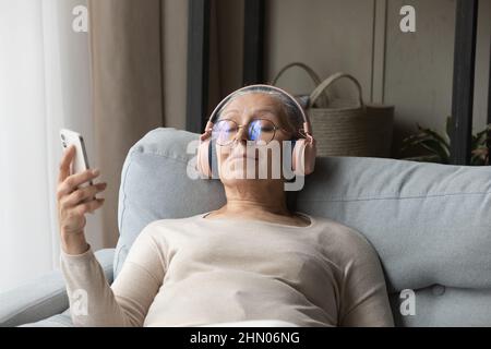 Calm senior lady in wireless headphones listening to relaxing music Stock Photo
