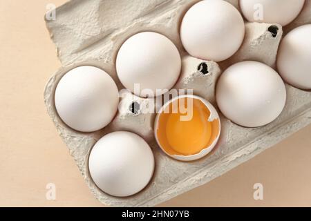 White eggs in a box, one with open shell showing the yellow egg yolk, ingredient for cooking, baking, and Easter, high angle view from above, selected Stock Photo
