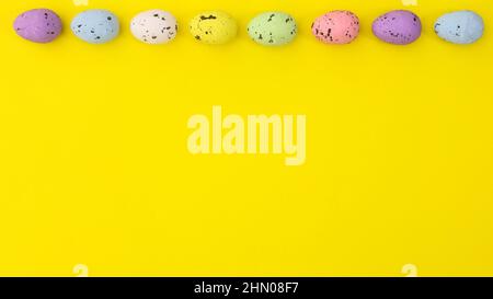 Easter vibrant colorful eggs on top of bright yellow background. Creative copy space. Flat lay minimal arrangement Stock Photo