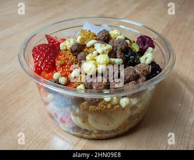 Greek yogurt topped with fresh fruits, nuts, granola, and cereals. Take-out dessert in a plastic bowl. Stock Photo