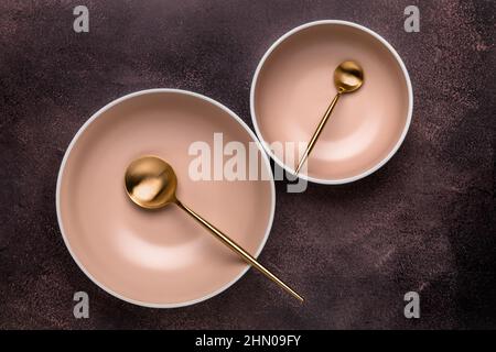 Two soup bowls and spoons on old dark brown table with scuffs. View from above. Dishes and utensils for serving and eating meals. Beige round rimmed p Stock Photo