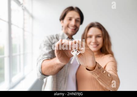 Glad happy caucasian young male and female in empty room with panoramic window, show keys Stock Photo