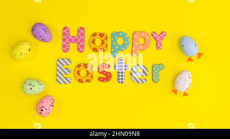 Happy Easter composition with text an colorful eggs on yellow background. Flat lay minimal spring scene Stock Photo