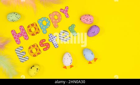 Happy Easter composition with text an colorful eggs and feathers on yellow background. Flat lay minimal spring scene Stock Photo