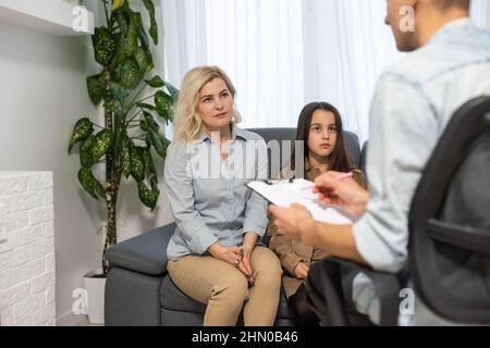 Female psychologist counseling parent. Serious single mom and sad unhappy child sitting on sofa and discussing social behaviour, ADHD disorder Stock Photo
