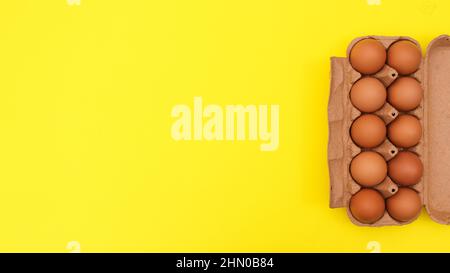 Card box with organic fresh eggs on right side of yellow background. Flat lay minimal Easter food. Stock Photo