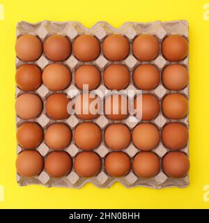 Organic eggs in cardboard box on vibrant yellow background. Flat lay Easter food Stock Photo