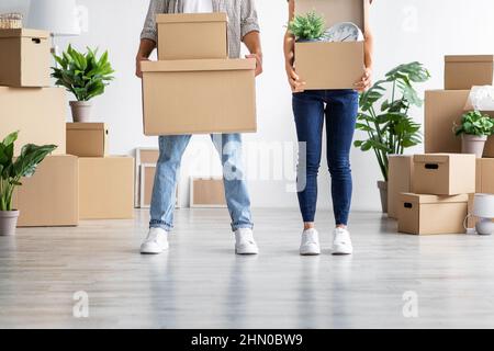 European young wife and husband in casual hold cardboard boxes with belongings, moving to new home Stock Photo