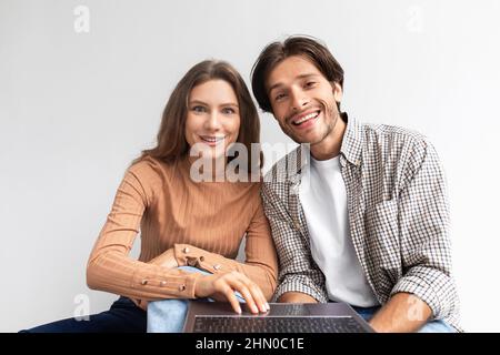 Smiling european young couple sit on floor in empty room look at computer and planning interior in new house Stock Photo