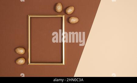 Golden frame with golden glitter eggs on pastel beige and brown background. Easter flay lay copy space Stock Photo