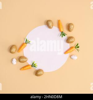 Easter paper card note with carrots and eggs for Easter on pastel beige background. Flat lay minimal composition Stock Photo