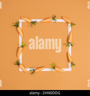 Easter scene with white frame and carrots on vibrant orange background. Flat lay minimal Stock Photo