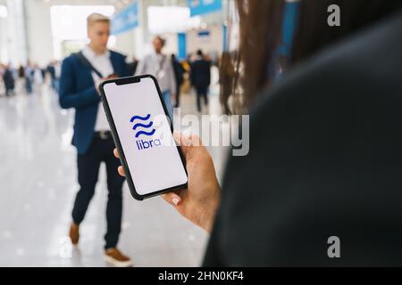 Woman hand holding iphone Xs with logo of Libra at a conference. Libra Facebook cryptocurrency and bitcoin cryptocurrency smartphone share, Libra coin Stock Photo