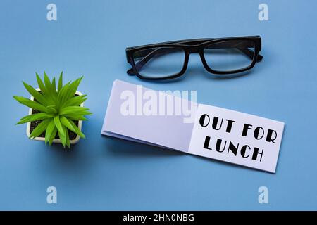Out for lunch text on notepad with reading glasses and potted plant. Directly above. Flat lay, Message and reminder concept. Stock Photo