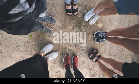 Legs and sneakers of teenage boys and girls standing in half circle on the sand. Stock Photo